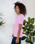 Side view of smiling woman wearing lilac Milk Sandwich T-shirt with DO GOOD slogan, standing near indoor plants, minimalist inspirational tee.