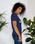 Side profile of smiling woman in navy Milk Sandwich T-shirt with DO GOOD text, standing near plants, casual inspirational graphic tee.