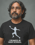 Man with glasses and long hair wearing black Milk Sandwich T-shirt with distressed football player graphic and text I Peaked in High School, nostalgic athletic tee.