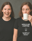 Two women wearing black t-shirts; one woman is smiling excitedly while the other drinks from a white mug and wears a shirt that says ‘Hold My Coffee I’m About To Prove You Wrong’ with a coffee cup graphic.