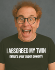 Excited man with glasses wearing black “I ABSORBED MY TWIN (What’s your superpower?)” t-shirt, smiling wide.