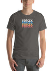 Man wearing a Milk Sandwich asphalt t-shirt with a colorful stacked relax text design in white, blue, orange, and pink distressed print.