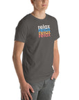 Angled front view of a man wearing a Milk Sandwich asphalt t-shirt with a colorful distressed relax text design repeated vertically in white, blue, orange, and pink.