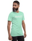 Side-facing man wearing heather mint Milk Sandwich t-shirt with distressed white text that reads SMILE! on the chest, set against a white backdrop.