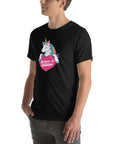 Young man wearing a black t-shirt with a colorful unicorn holding a pink heart that says “Believe in Edibles,” standing with hands in pockets, side view.