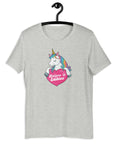 Light grey t-shirt on a hanger with a colorful unicorn graphic above a pink heart that says “Believe in Edibles.”