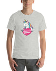 Man wearing a light grey t-shirt with a colorful unicorn holding a pink heart that says “Believe in Edibles,” standing facing forward with one hand relaxed and the other in his pocket.