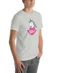 Young man wearing a light grey t-shirt with a colorful unicorn holding a pink heart that says “Believe in Edibles,” standing with hands in pockets, side view.