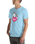 Young man wearing a ocean blue t-shirt with a colorful unicorn holding a pink heart that says “Believe in Edibles,” standing with hands in pockets, side view.