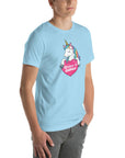 Young man wearing a ocean blue t-shirt with a colorful unicorn holding a pink heart that says “Believe in Edibles,” standing with hands in pockets, side view.
