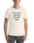 Man wearing white “DON’T BE A PEE PEE POO POO HEAD” t-shirt, standing casually with hands by pockets.