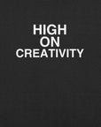Close-up of black t-shirt fabric with the phrase “HIGH ON CREATIVITY” printed in bold white uppercase letters in three lines.