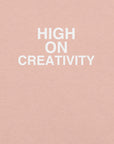 Close-up of peach t-shirt fabric with the phrase “HIGH ON CREATIVITY” printed in bold white uppercase letters in three lines.