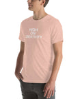 Man wearing a peach t-shirt with white text ‘HIGH ON CREATIVITY’, standing sideways with one hand in pocket