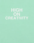 Close-up of mint t-shirt fabric with the phrase “HIGH ON CREATIVITY” printed in bold white uppercase letters in three lines.