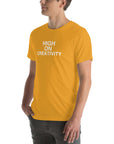 Man wearing a mustard t-shirt with white text ‘HIGH ON CREATIVITY’, standing sideways with one hand in pocket