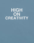 Close-up of steel blue t-shirt fabric with the phrase “HIGH ON CREATIVITY” printed in bold white uppercase letters in three lines.