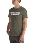 Man wearing army “I ABSORBED MY TWIN (What’s your super power?)” t-shirt, standing sideways with hands in pockets.