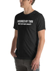 Man wearing black “I ABSORBED MY TWIN (What’s your super power?)” t-shirt, standing sideways with hands in pockets.