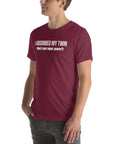 Man wearing maroon “I ABSORBED MY TWIN (What’s your super power?)” t-shirt, standing sideways with hands in pockets.