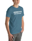 Man wearing teal “I ABSORBED MY TWIN (What’s your super power?)” t-shirt, standing angled to the side with hands in pockets.