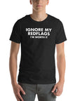 Man wearing black “IGNORE MY RED FLAGS I’M WORTH IT” t-shirt, standing casually with hands by pockets.