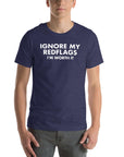 Man wearing navy “IGNORE MY RED FLAGS I’M WORTH IT” t-shirt, standing casually with hands by pockets.