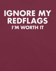 Close-up of maroon t-shirt with bold white text “IGNORE MY RED FLAGS I’M WORTH IT” printed on the front.