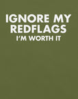 Close-up of olive t-shirt with bold white text “IGNORE MY RED FLAGS I’M WORTH IT” printed on the front.