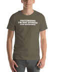 Man wearing army “PRETENDING I’M NOT STONED IS MY SUPERPOWER” t-shirt, standing casually with hands by pockets.