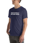 Man wearing a navy “THAT’S WHAT SHE/HER SAID” t-shirt, standing with hands in pockets, looking to the side.