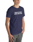 Man wearing navy “THAT’S WHAT SHE/HER SAID” t-shirt, standing casually with one hand in pocket, looking slightly to the side