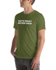 Man wearing a olive “THAT’S WHAT SHE/HER SAID” t-shirt, standing with hands in pockets, looking to the side.