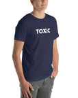 Man wearing navy “TOXIC” t-shirt, standing with hands in pockets, looking slightly to the side.