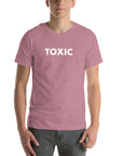 Man wearing orchid “TOXIC” t-shirt, standing straight with hands relaxed by pockets, facing forward.