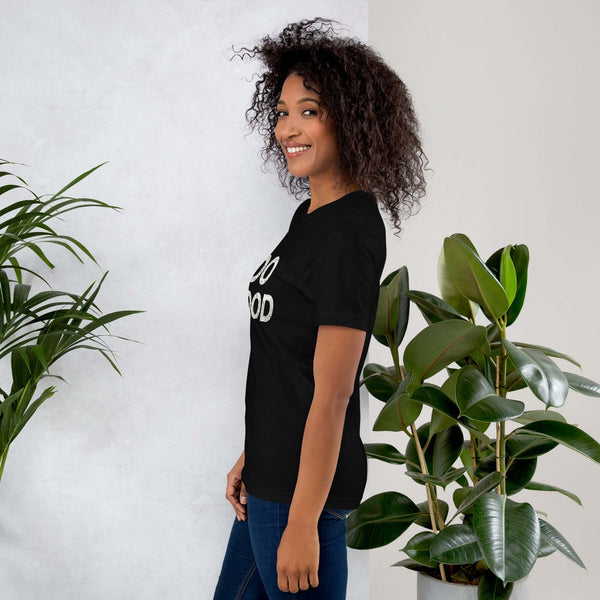 Side view of smiling woman wearing black Milk Sandwich T-shirt with DO GOOD slogan, standing near indoor plants, minimalist inspirational tee.