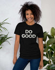 Smiling woman wearing black Milk Sandwich T-shirt with distressed white DO GOOD text, standing indoors next to plants, casual inspirational tee.