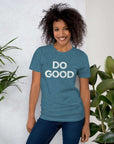 Smiling woman wearing teal Milk Sandwich T-shirt with distressed white DO GOOD text, standing indoors next to plants, casual inspirational tee.