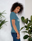 Side profile of smiling woman in teal Milk Sandwich T-shirt with DO GOOD text, standing near plants, casual inspirational graphic tee.