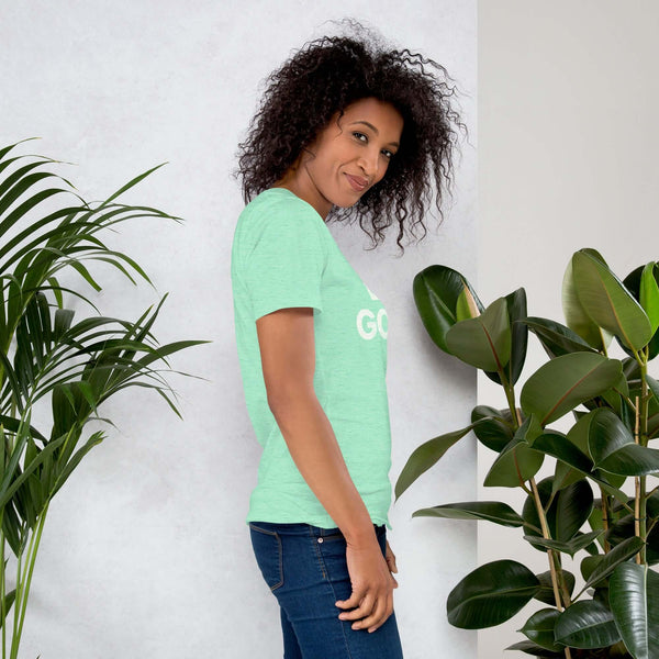 Side profile of smiling woman in heather mint Milk Sandwich T-shirt with DO GOOD text, standing near plants, casual inspirational graphic tee.