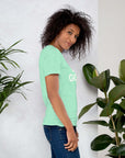 Side profile of smiling woman in heather mint Milk Sandwich T-shirt with DO GOOD text, standing near plants, casual inspirational graphic tee.