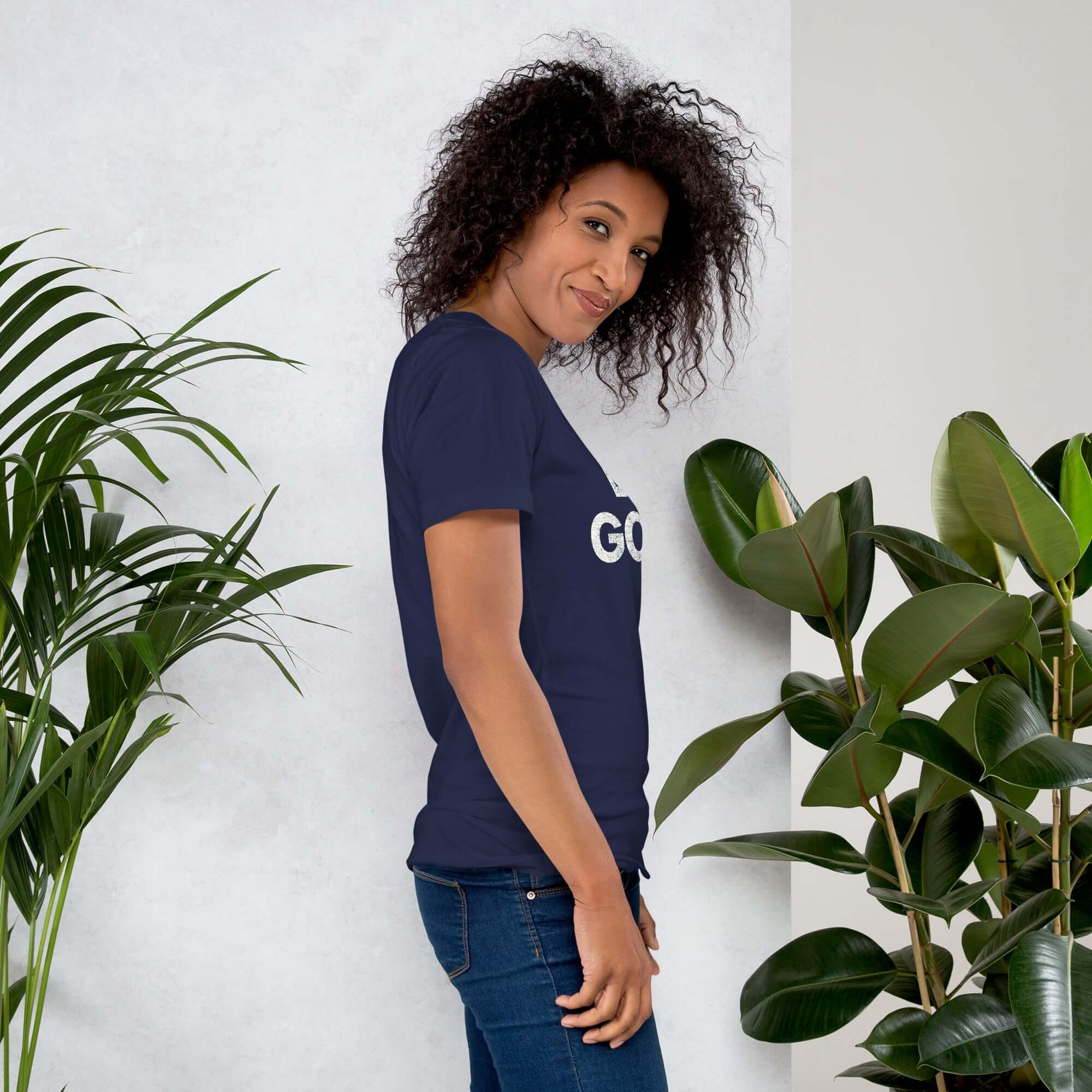 Side profile of smiling woman in navy Milk Sandwich T-shirt with DO GOOD text, standing near plants, casual inspirational graphic tee.