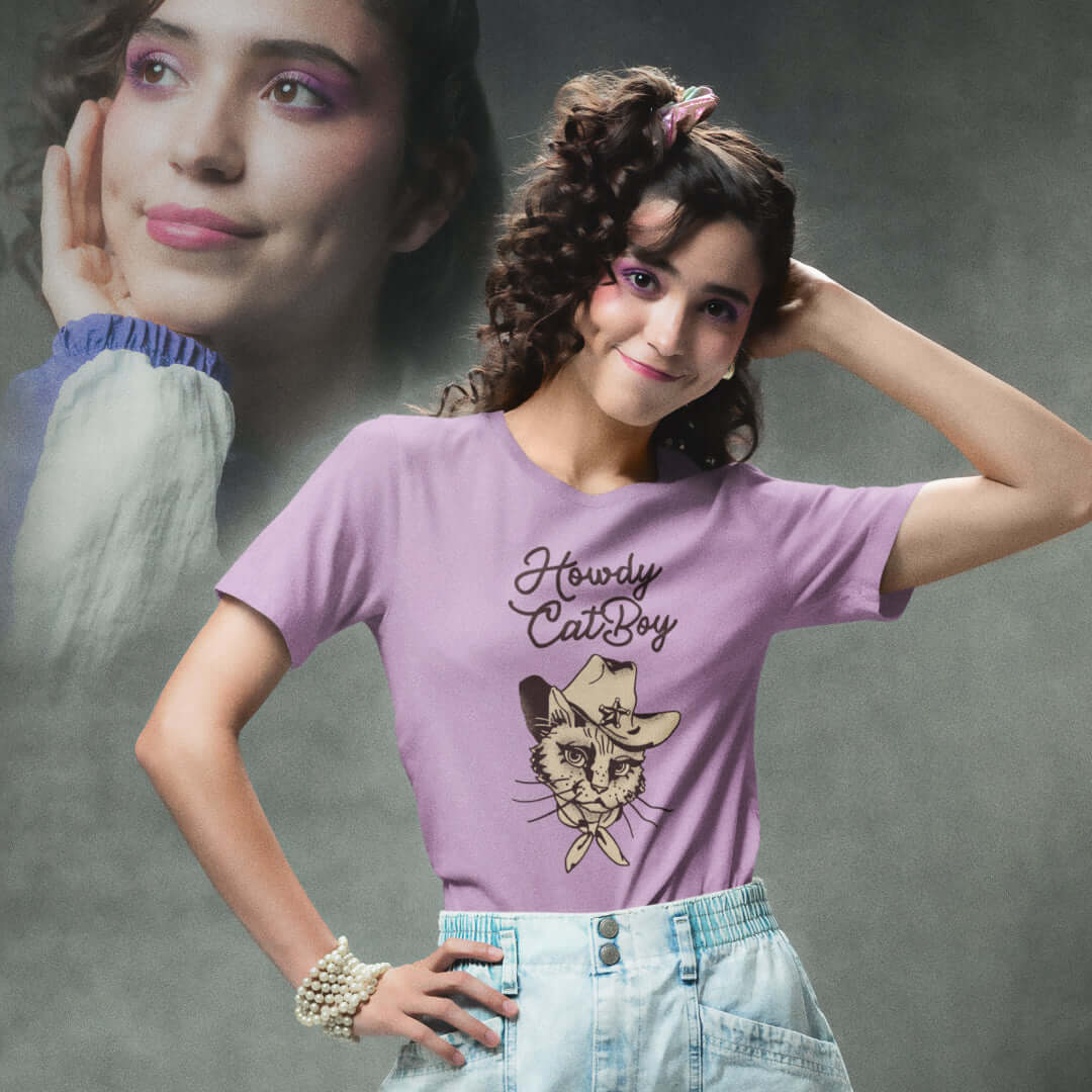 Smiling young woman in pink Milk Sandwich T-shirt with Howdy CatBoy text and illustrated cowboy cat graphic, retro-inspired pastel aesthetic.