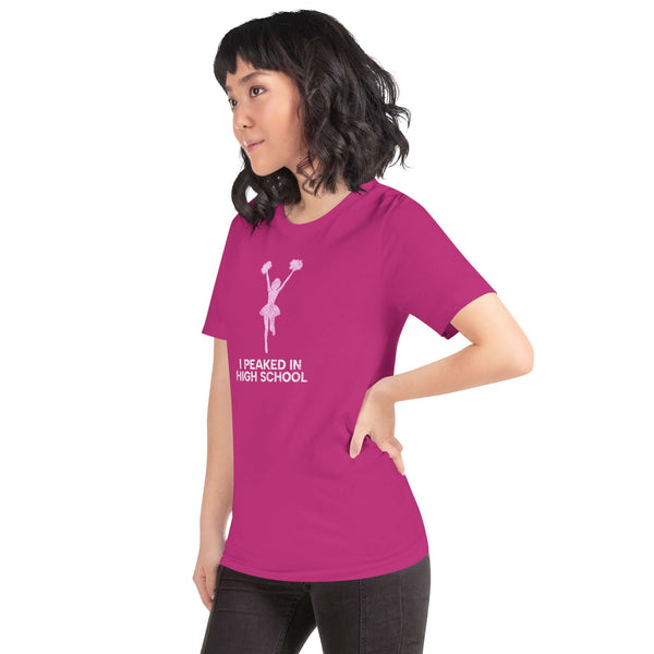 Model wearing a vibrant berry unisex Milk Sandwich T-shirt  that says "I Peaked in High School" with a cheerful cheerleader graphic.
