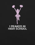 Close-up of black Milk Sandwich T-shirt with distressed pink cheerleader graphic and white text that reads I Peaked in High School, sarcastic retro tee.