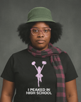 Serious woman in hat and scarf wearing black Milk Sandwich T-shirt with faded pink cheerleader graphic and text I Peaked in High School, ironic retro tee.