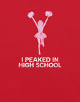 Close-up of red Milk Sandwich T-shirt with distressed pink cheerleader graphic and white text that reads I Peaked in High School,  sarcastic retro tee.