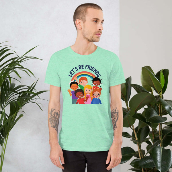 Man wearing a light mint Milk Sandwich t-shirt featuring a colorful illustration of six diverse cartoon kids smiling under a rainbow with the text "LET'S BE FRIENDS" standing indoors next to large green plants.