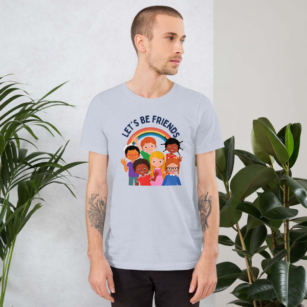 Man wearing a light blue Milk Sandwich t-shirt featuring a colorful illustration of six diverse cartoon kids smiling under a rainbow with the text "LET'S BE FRIENDS" standing indoors next to large green plants.
