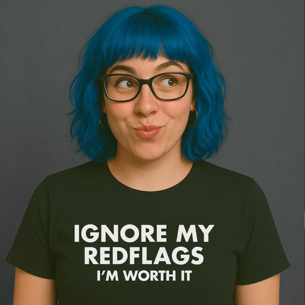 Woman with blue hair and glasses wearing a black “IGNORE MY RED FLAGS I’M WORTH IT” t-shirt, looking cheeky.